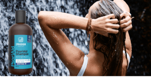 Sphagnum Botanicals Psoriasis Shampoo bottle beside a woman standing with her back to the camera, hands in her wet hair, in front of a waterfall