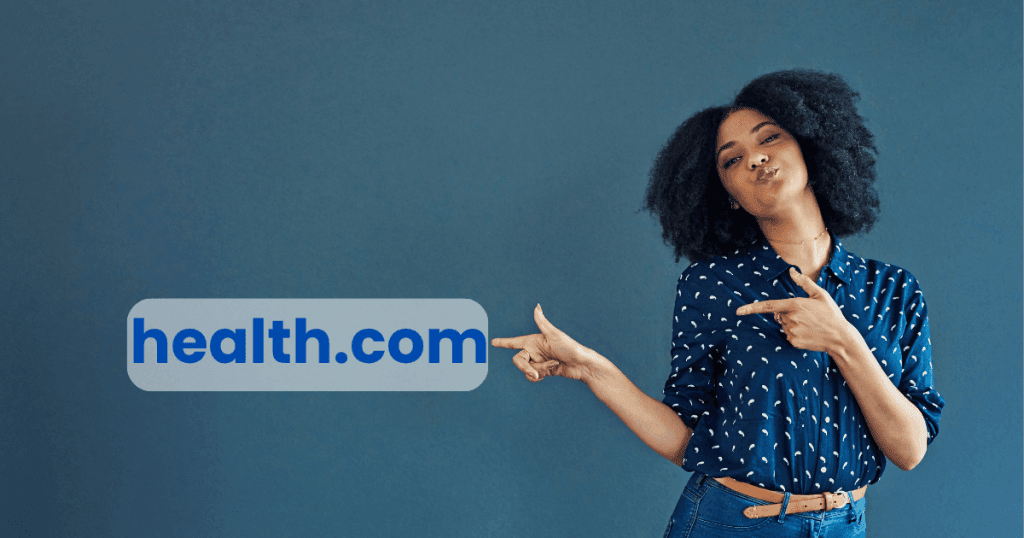 Afro curly-haired woman smiling and pointing toward a Health.com sign with a playful, confident smirk on a grey background.